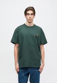 Tmavě zelené bavlněné tričko s krátkým rukávem, kulatým výstřihem a malým vyšitým logem na hrudi. Měkká textura s volným střihem.