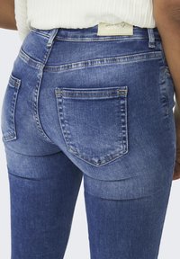 Jean bleu taille haute avec un délavage usé, deux poches arrière et des coutures contrastantes le long des coutures.