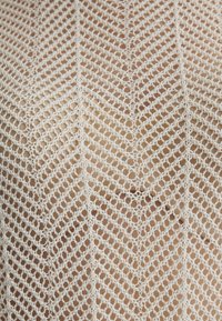 Weißes gehäkeltes Top mit einem Zickzackmuster, das ein offenes Strickdesign und eine strukturierte Oberfläche aufweist, die die Komplexität der Garnverarbeitung hervorhebt.