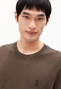 Braunes Baumwoll-T-Shirt mit rundem Halsausschnitt und kurzen Ärmeln. Verfügt über ein dezentes Logo auf der Brust und eine glatte Textur.