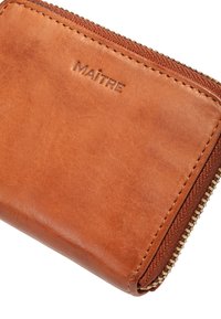 Brown leather wallet with a zip closure, textured surface, and embossed "MAÎTRE" logo. Golden zipper and stitching detail visible.