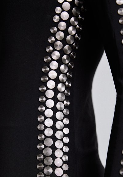 Black garment with a row of shiny, textured silver studs arranged vertically. The studs vary in size, creating a notable pattern along the fabric.