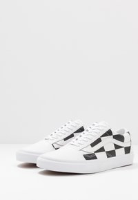 Baskets en toile blanche avec motif damier noir sur les côtés, semelle en caoutchouc blanche plate et lacets blancs étroits.