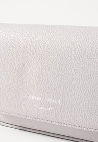 Portafoglio in pelle grigio chiaro texturizzata con marchio in rilievo, cuciture sobrie e finitura liscia. Forma rettangolare compatta.