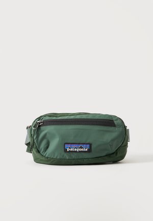 Zielona nerka Patagonia z przednią kieszenią na zamek i naszywką z logo, prezentowana na białym tle.