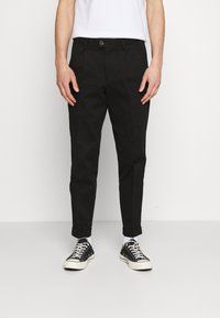 Black pants with a straight fit, made of cotton, featuring a button closure, front pockets, and rolled cuffs. Worn with black sneakers.