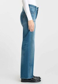 Jeans dritti azzurri realizzati in denim, con un taglio classico, cuciture sulle tasche posteriori e una texture liscia. Indossati con scarpe nere.