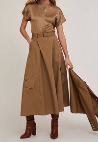 Blouse satinée beige avec manches courtes et détails boutons, assortie à une jupe taille haute en ligne A avec grandes poches plaquées.