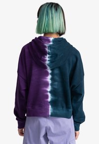 Sudadera con capucha con diseño tie-dye, dividida en colores morado y verde azulado, con un ajuste relajado y puños acanalados para mayor textura.