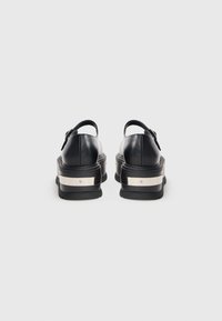 Black platform sandals with thick soles featuring silver metallic bands, viewed from the back, on a plain light background.