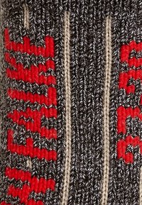 Gros plan sur un tissu tricoté gris foncé avec des motifs verticaux rouges et beiges, et des détails de couture côtelés texturés.