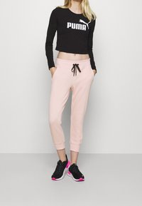 Svart kortärmad långärmad tröja med "PUMA"-logotyp, tillsammans med rosa sweatpants med dragsko i midjan och sidofickor, avslutat med svarta sportskor.