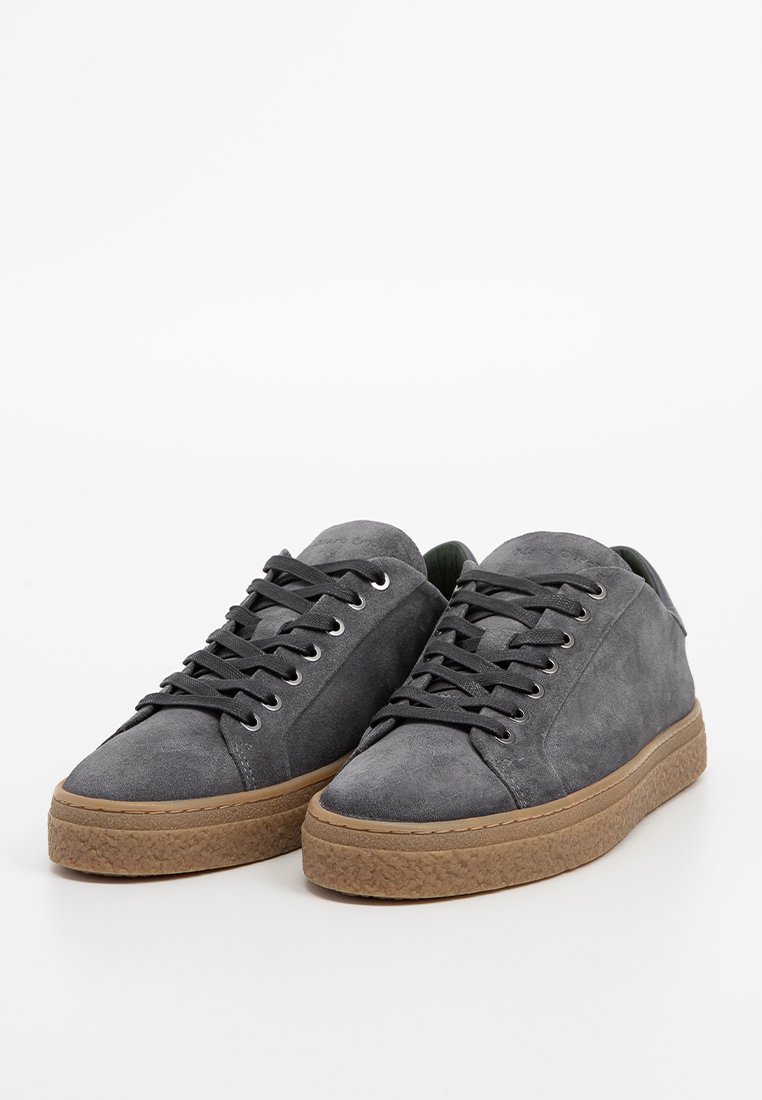 Szare zamszowe sneakersy z czarnymi sznurowadłami, charakteryzujące się teksturowaną, karmelową gumową podeszwą oraz minimalistycznym designem. Okrągły nos i gładkie wykończenie.
