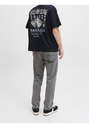 Person wearing black graphic T-shirt with building and text "1932 RANDLUX ESTATES" on back, gray jeans, and black sneakers.