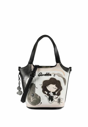 Kleine schwarz-weiße Handtasche mit einem Design eines Cartoon-Mädchen-Dirigenten, schwarzen Griffen und dekorativen hängenden Anhängern an der Seite.