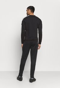 Svart sweatshirt med hvite side-striper, kombinert med svarte joggebukser. Stoffene ser glatte ut og har en avslappet passform, designet for komfort.
