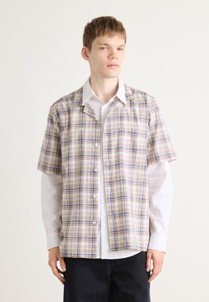 Short-sleeve button-up shirt in beige with blue and brown plaid pattern; layered over a white long-sleeve shirt; relaxed fit.