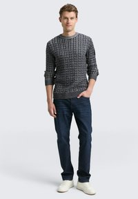 Grauer Strickpullover mit strukturiertem Muster, Rundhalsausschnitt und langen Ärmeln, kombiniert mit dunkelblauen Jeans und weißen Sneakers.