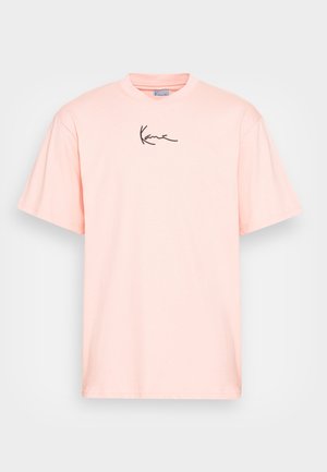 Jasnoróżowa bawełniana koszulka z okrągłym dekoltem i krótkimi rękawami, z czarnym logo sygnaturowym na przodzie. Gładka tekstura, standardowy krój.