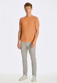 Suéter de punto corto de manga con textura de color naranja claro, combinado con pantalones de chándal ajustados grises y zapatillas blancas.