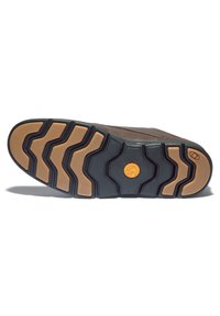 Semelle de chaussure avec des rainures profondes en caoutchouc noir et fauve, comportant un logo circulaire Timberland près du centre et un logo hexagonal près du talon.