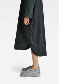 Robe longue vert foncé texturée avec fentes sur les côtés, associée à des chaussures à plateforme grises épaisses avec une finition lisse et un détail de bride.