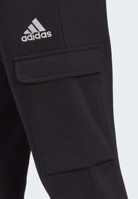 Sorte cargo bukser lavet af en bomuldsblandet stof, med en stor sidelomme og et metallic sølv Adidas-logo broderet på den øverste lår.