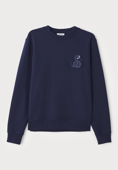 Tummansininen collegepaita, joka on valmistettu pehmeästä kankaasta. T-paidassa on koristeellinen käärmeembroidointi vasemmassa rinnassa sekä joustavat hihansuut ja helma.