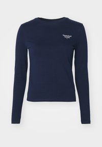 Tumedate pikkade varrukatega puuvillane T-särk ümmarguse kaelusega, millel on vasakul rinnal väike valge "Tommy Jeans" logo. Lihtne disain, ilma mustriteta.