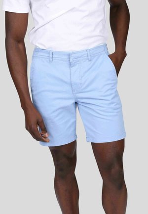 Shorts en coton bleu clair avec une taille plate, des poches latérales et un ourlet retroussé. Portés avec un T-shirt blanc à col rond.