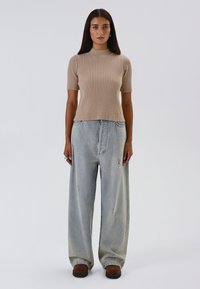 Top beige a coste con maniche corte; abbinato a jeans larghi in denim chiaro strappati e scarpe slip-on marroni scure.
