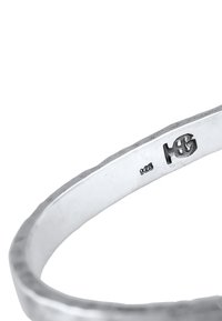 Armband av sterling silver med hamrad yta, med en slät innersida och graverade stämplar på ena sidan.