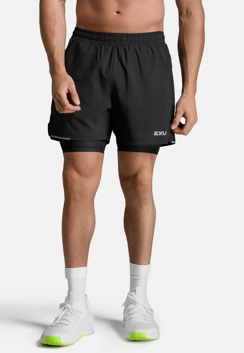 Zwarte atletische korte broek met een strikkoord in de taille, voorzien van een binnenvoering en zilveren accenten, gecombineerd met witte en neon groene sneakers.