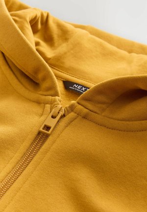 Gelbe Zip-Hoodie mit weicher Textur, ausgestattet mit einem Frontreißverschluss und einer enganliegenden Kapuze. Markenlabel im Kragen sichtbar.