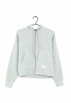 Sweat à capuche zippé Adidas gris clair avec poches avant, capuche avec cordons et logo en bas à gauche, suspendu sur un cintre noir.