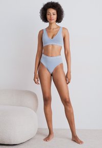 Světle modrý žebrovaný crop top a vysoké kalhotky s logem. Měkký materiál, přiléhavý střih a minimální švy.
