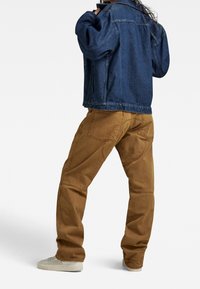 Jeansjacka i mörkblått, lös passform, tillsammans med beige kordbyxor med fickor. Vita sneakers fulländar looken.