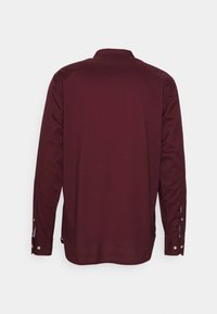 Camisa de manga larga burdeos con cuello, puños de botón y tejido texturizado. La vista trasera muestra líneas suaves y sin patrones.