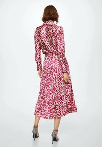 Robe à manches longues en rose et crème avec un motif floral, dotée d'une taille ceinturée et d'une jupe plissée. Le tissu semble lisse et léger.