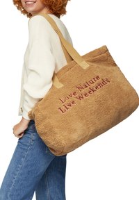 Brązowa, pluszowa torba na ramię o miękkiej teksturze. Zawiera haftowany czerwony napis: "Kochaj naturę, przeżywaj weekendy". Posiada długie beżowe paski do noszenia.