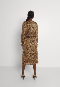 Brun leopardmönstrad klänning med lång ärm, åtsittande midja och volangärmar, tillverkad av ett lätt, semi-genomskinligt tyg.