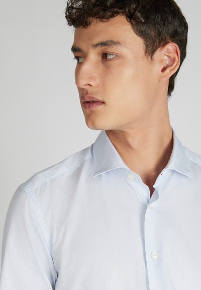 Camicia botton-down azzurro chiaro con colletto italiano e sottili righe verticali. Presenta una texture liscia e bottoni bianchi sul davanti.