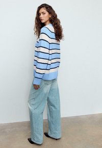 Maglione a righe azzurro chiaro con larghe strisce blu scuro e crema. Abbinato a jeans di denim larghi e sbiaditi e scarpe nere appuntite.