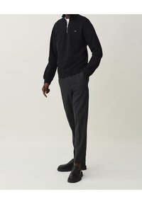 Schwarzer Reißverschluss-Sweatshirt, graue strukturierte Hose und schwarze Slipper. Lässige Passform mit geripptem Saum und Schulterdetails.