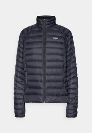 Casaco acolchoado azul marinho com zip frontal, gola alta e dois bolsos laterais. Apresenta secções acolchoadas e um logótipo da Patagonia no peito.
