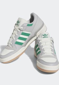 Nízké tenisky Adidas v bílé a světlé šedé barvě se zelenými pruhy a logem, off-white tkaničkami a gumovými podrážkami.