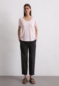 Lichtroze, kort mouw t-shirt, relaxte pasvorm; gecombineerd met zwarte, taps toelopende broeken en zwarte sandalen met gouden hardware-accenten.