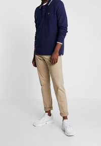 Marinblå långärmad polo med vit krage, beige smalbyxor och vita sportskor, som framhäver en avslappnad outfit.