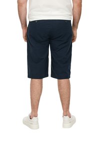 Shorts en coton bleu marine avec une coupe décontractée, dotés de poches arrière à boutons et d'un ourlet juste au-dessus du genou, associés à des baskets blanches.