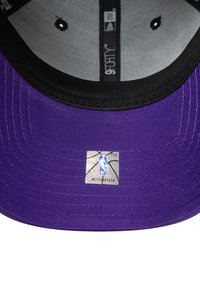 Cappello da baseball viola con visiera nera, dotato di un'etichetta metallica con il logo NBA e etichetta 9FORTY all'interno, tessuto texturizzato e dettagli di cucitura.